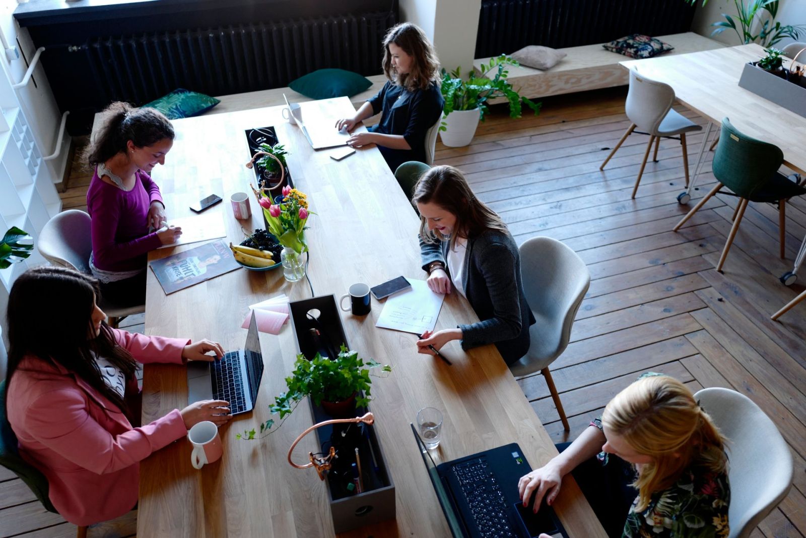 An overhead view of people working at a shared coworking table with laptops