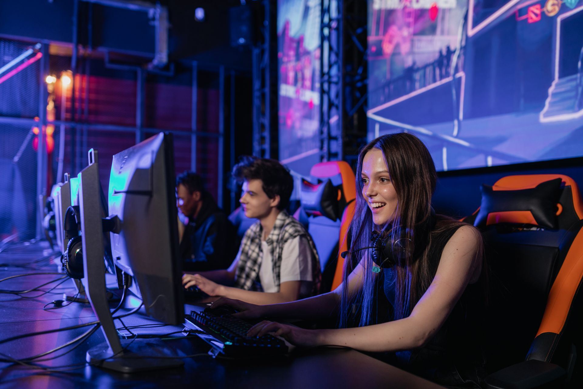 Players at gaming PCs mid-match, with a giant screen lit up behind them