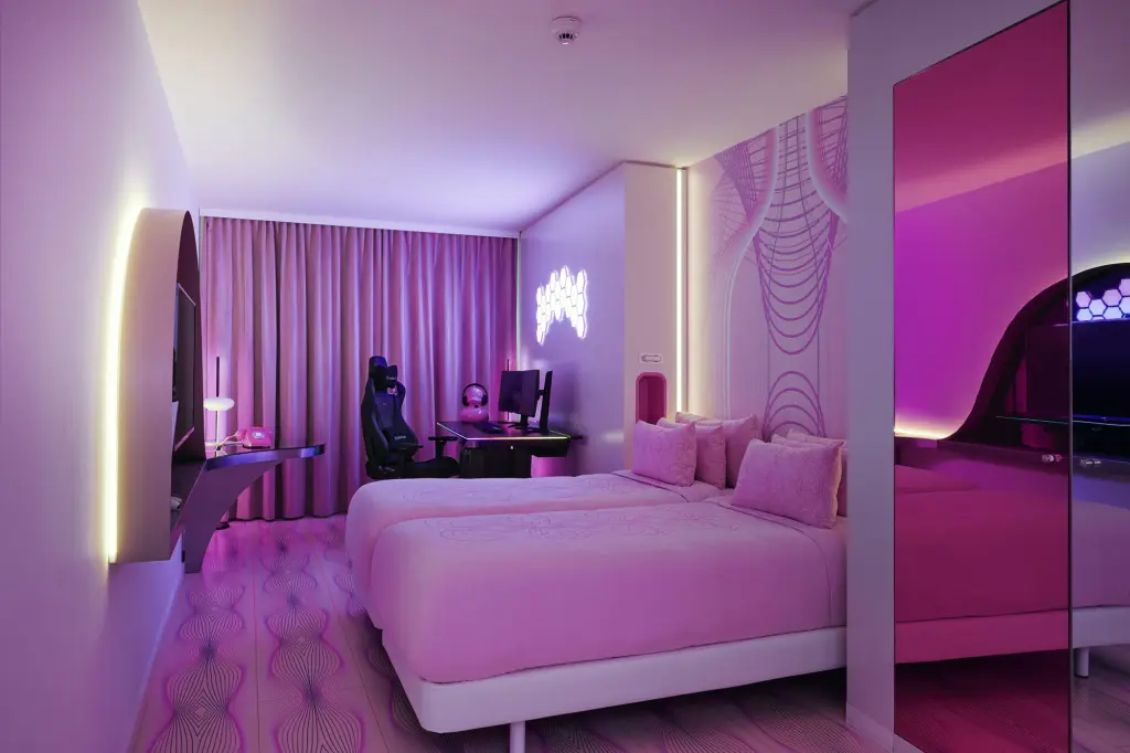 A pink neon-themed hotel room with a gaming desk and chair